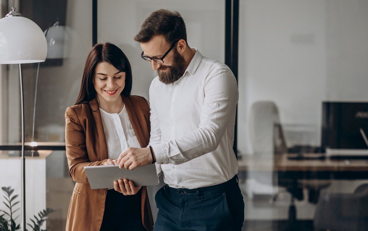 Smiling coworkers reviewing project details on a tablet in a modern office setting, highlighting teamwork and collaboration.
